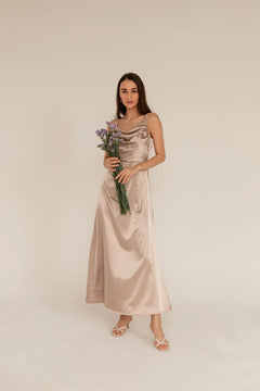 A woman in a beige satin dress with a water neckline and thin straps, holding a bouquet of flowers.